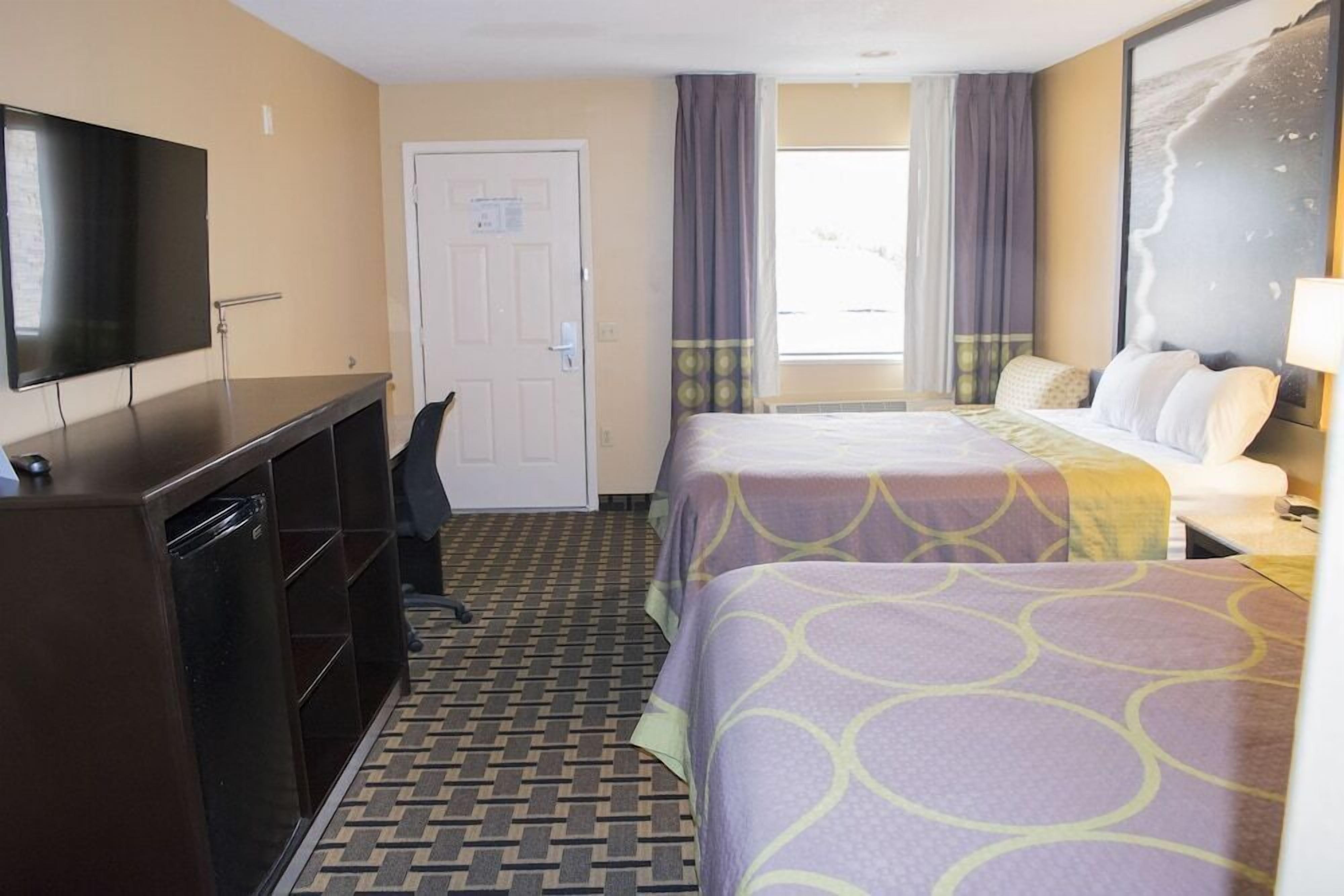 A hotel room with a bed, a desk, a TV, and a door.