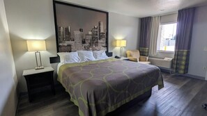 A hotel room with a bed, two bedside tables, a chair, a cityscape artwork on the wall, and a window with curtains. - Houston/willowbrook/hwy 249 (Houston)