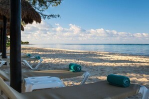 Une plage avec des chaises longues et des serviettes, une structure dotée d’un toit de chaume et une vue sur la mer.