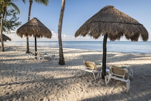 Una playa con sombrillas de paja, sillas de descanso y palmeras.