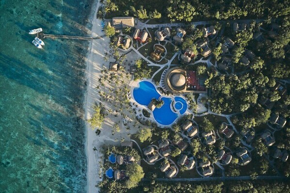 Vue aérienne d’un complexe hôtelier doté de plusieurs piscines, d’une plage et d’un port de plaisance.