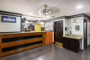 Un hall d’hôtel avec un comptoir d’accueil en bois, un ventilateur de plafond, une horloge et un panneau Super 8.