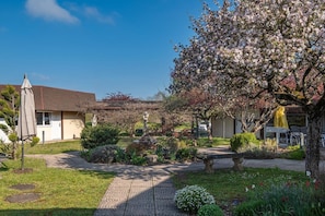 A garden with a paved walkway, a reception desk, and a building with a sloped roof. - Charme Hotel Montbeliard Sud (Arbouans)