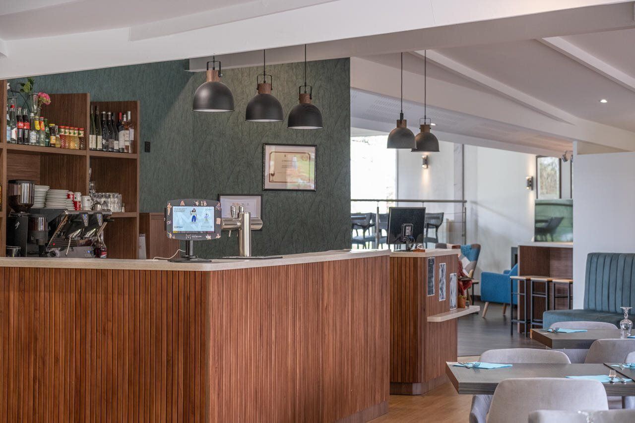 A modern bar area with wooden paneling, pendant lighting, and a digital screen.