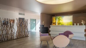 Zona d'arribada amb un disseny modern, que inclou una taula d'informació, dues cadires i una paret decorativa amb art abstracte.