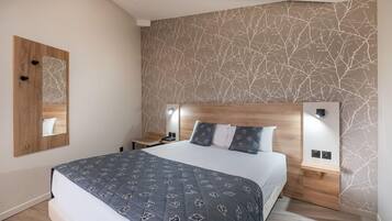 A bedroom with a bed, bedside tables, a nightstand, a mirror, and a wall with a leaf pattern.