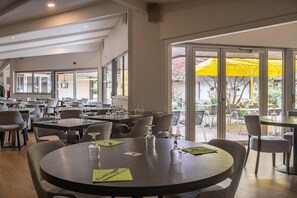 A restaurant with round tables, chairs, and outdoor seating with yellow umbrellas. - Charme Hotel Montbeliard Sud (Arbouans)