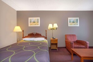 A hotel room with a bed, two bedside lamps, a chair, a table, and two framed pictures on the wall. - Rodeway Inn Glade Spring (Glade Spring)