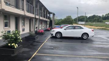 A parking lot with a white car parked in front of a building with multiple windows and balconies.