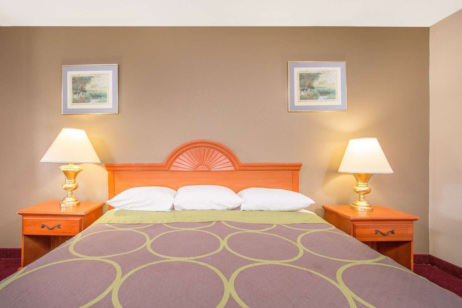A hotel room with a bed, two nightstands, two lamps, and two framed pictures on the wall.