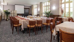 A conference room with multiple tables and chairs, a projector screen, and large windows. - The Originals City, Hotel Bristol, Le Puy-en-velay (Le Puy-en-Velay)