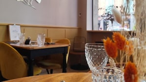 A restaurant interior with a wooden table, chairs, decorative wall art, and a window with a view. - The Originals City, Hotel Bristol, Le Puy-en-velay (Le Puy-en-Velay)