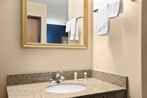 A bathroom with a granite countertop sink, a mirror with a gold frame, and white towels on a towel rack. - Hudson Hotel (Hudson)