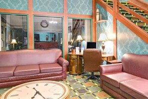 A room with a large clock, two leather sofas, a desk with a computer, and a staircase. - Hudson Hotel (Hudson)