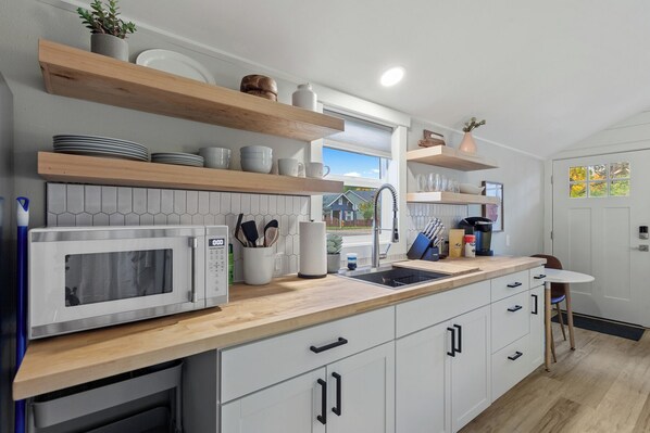 A modern kitchen with white cabinets, a microwave, a sink, and wooden shelves. - Quiet Studio Getaway in the Heart of Coeur d'Alene (Coeur d'Alene)