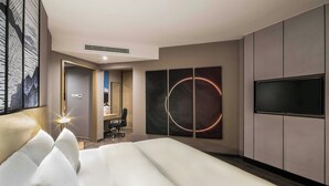 A modern hotel room with a large bed, a flat-screen TV, and a circular artwork on the wall. - Aber Unaiza (Unaizah)