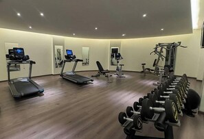 Un gimnasio con cintas de correr, una prensa de banca y un estante con mancuernas.