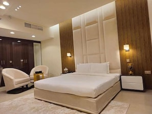 Quarto moderno com uma cama grande, duas mesas de cabeceira, uma cadeira e um guarda-roupa.