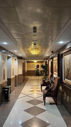 Un vestíbulo de hotel con piso a cuadros, una araña y obras de arte enmarcadas en las paredes, junto con un mostrador de recepción.