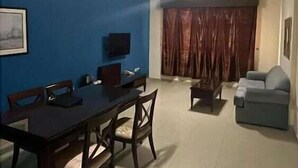 Un área de comedor con una mesa y sillas, un televisor en la pared y un sofá en la sala.