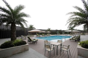 Ein Poolbereich mit Liegestühlen und Sonnenschirmen, umgeben von Palmen und einer Holzterrasse.