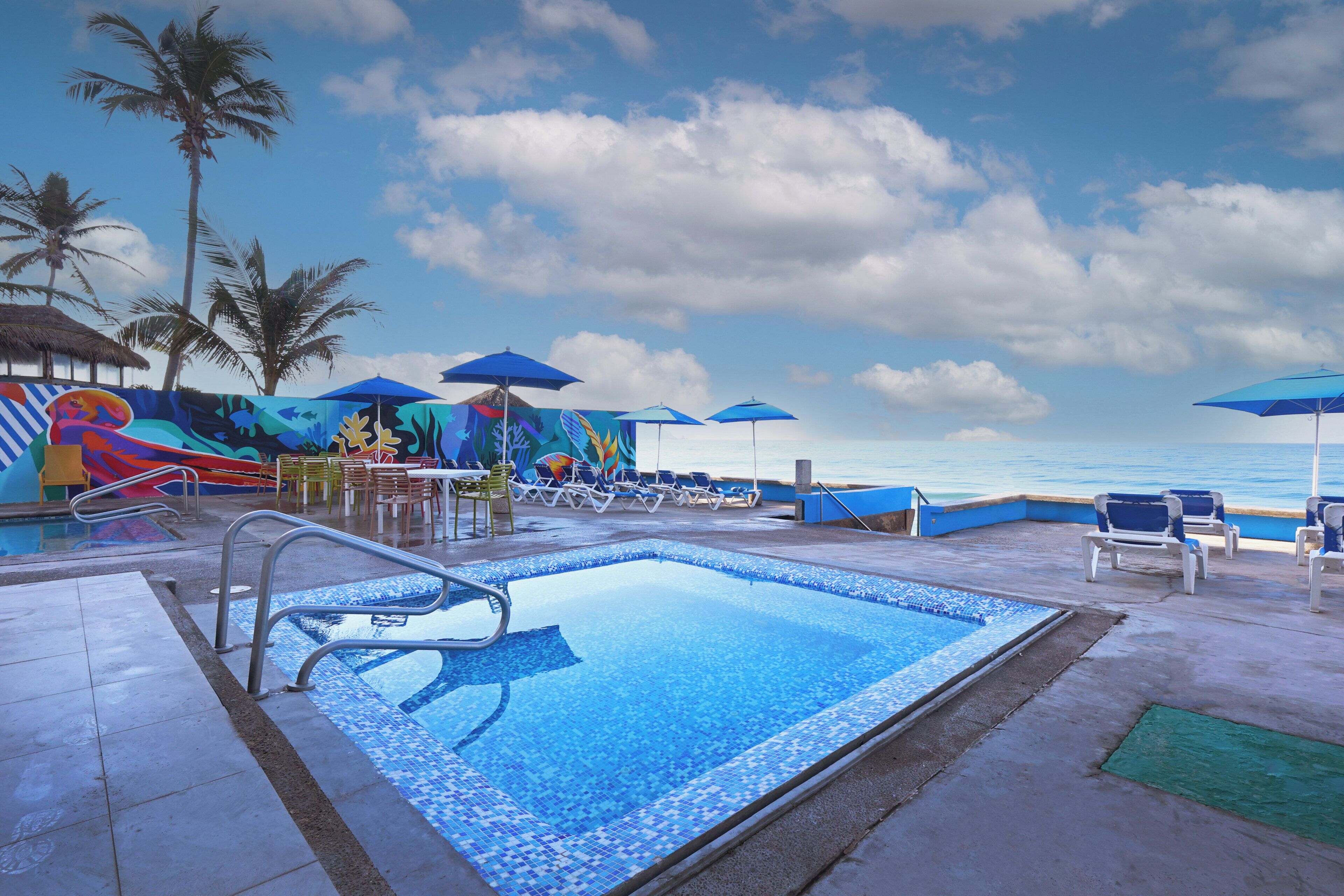 A pool area with lounge chairs and umbrellas, a slide, and a mural.