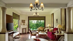 Amplio salón con chimenea, televisor, mesa de comedor con fruta y un ventanal con vistas al verdor.