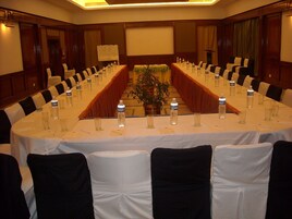 Una sala de conferencias con una larga mesa, sillas, botellas de agua y una planta.