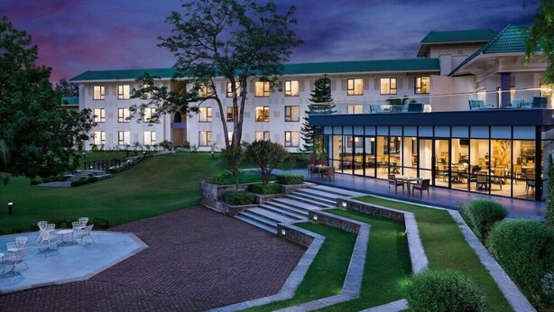 Un hotel con un jardín bien cuidado, zona de estar exterior y un edificio moderno con grandes ventanales.