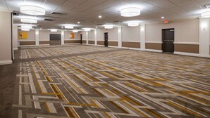 A large, empty hotel conference room with patterned carpet, recessed lighting, and a plain wall with a door. - Best Western Premier Airport/expo Center Hotel (Louisville)