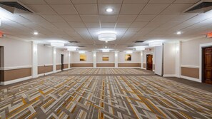 Uma sala de conferências ampla e bem iluminada, com carpete estampado, iluminação embutida e obras de arte emolduradas nas paredes.