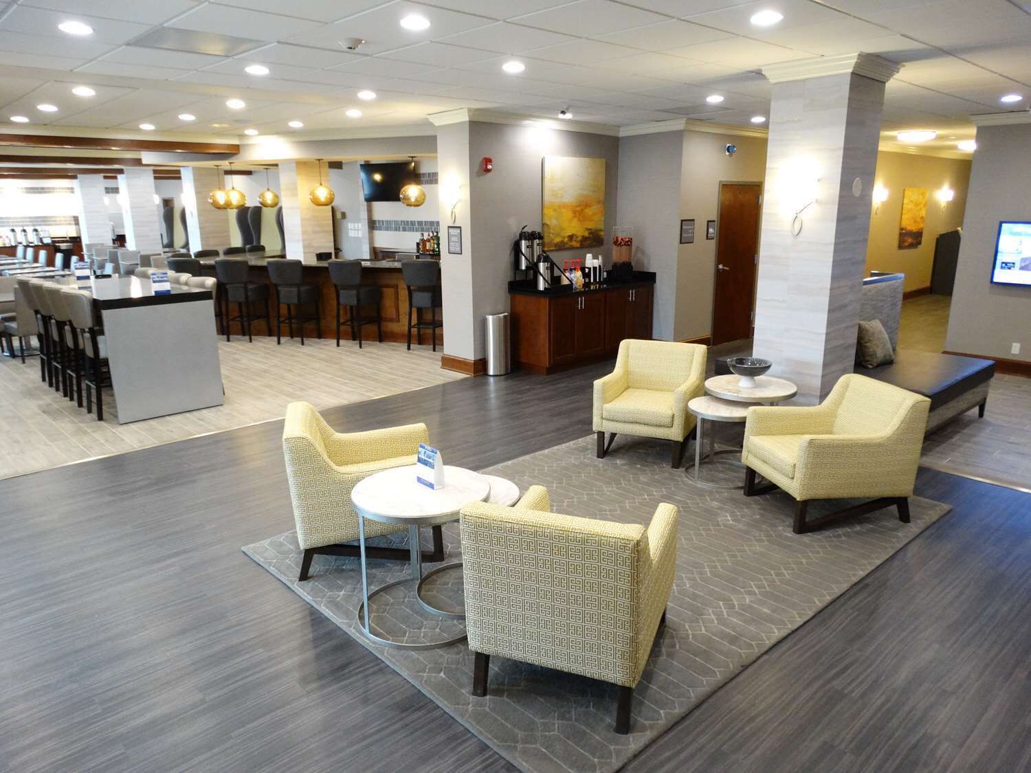 Un vestíbulo de hotel con zona de bar, disposición de asientos y mostrador de recepción.