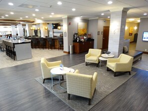 Um saguão de hotel com área de bar, assentos e balcão de recepção.