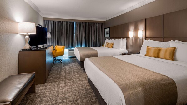 Ein Hotelzimmer mit zwei Betten, einem Schreibtisch mit Lampe, einem Sessel und einem Fernseher.