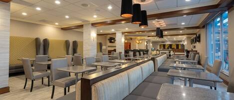A modern restaurant with high ceilings, recessed lighting, and a mix of booths and tables.