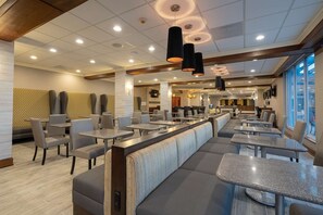 Un restaurant moderne avec de hauts plafonds, un éclairage encastré et un mélange de banquettes et de tables.