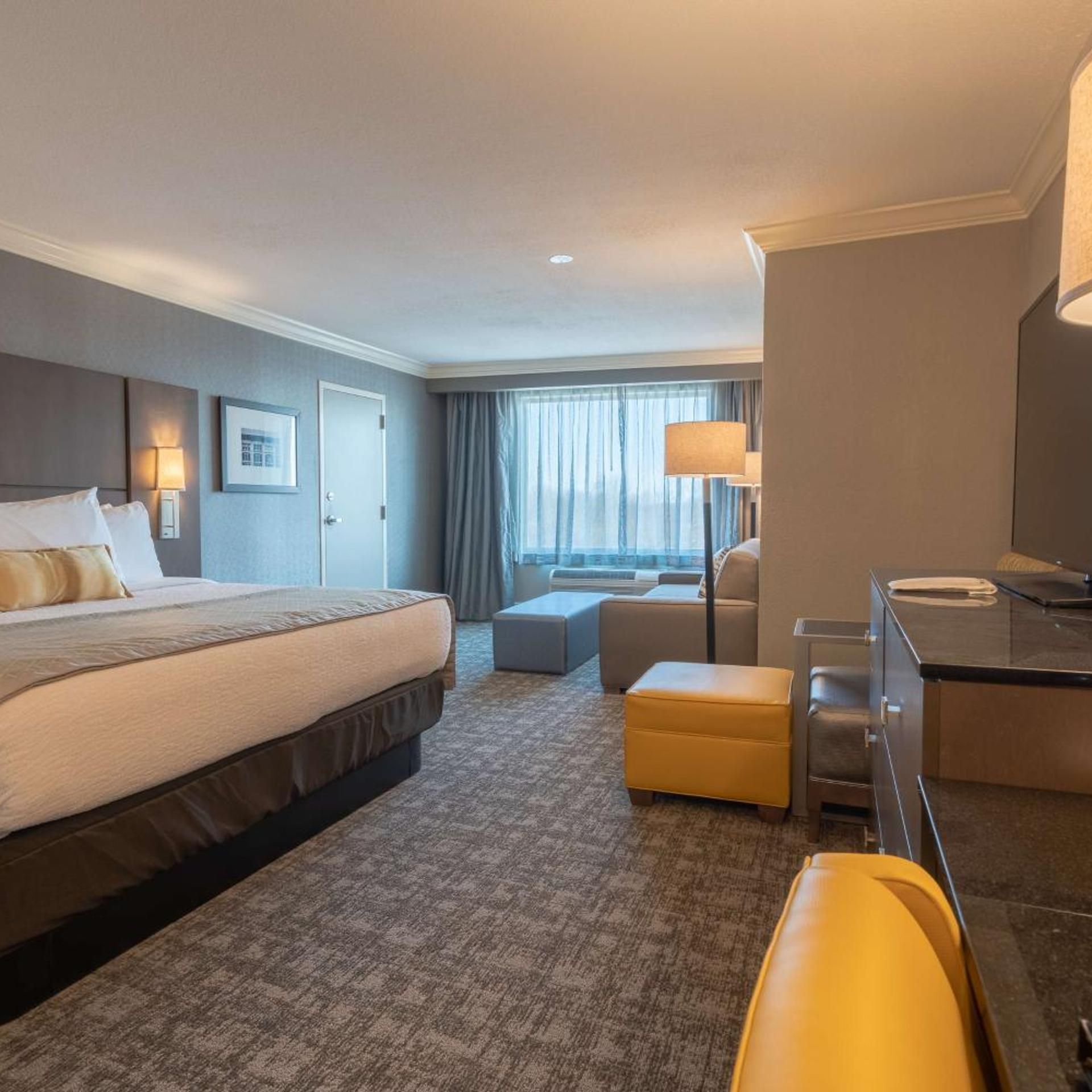 A hotel room with a bed, a desk, a chair, a sofa, and a window with curtains.