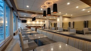A modern restaurant with booths and tables, a kitchen area, and a view through large windows. - Best Western Premier Airport/expo Center Hotel (Louisville)