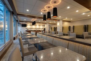 A modern restaurant with booths and tables, a kitchen area, and a view through large windows. - Best Western Premier Airport/expo Center Hotel (Louisville)