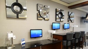 A reception desk with multiple monitors, a mirror, and a seating area with chairs. - Best Western Premier Airport/expo Center Hotel (Louisville)