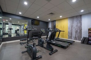 Une salle de sport équipée de tapis de course, de vélos elliptiques et d’un mur recouvert de miroirs.