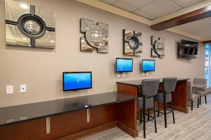 A reception area with a wooden counter, multiple monitors, and a TV. - Best Western Premier Airport/expo Center Hotel (Louisville)