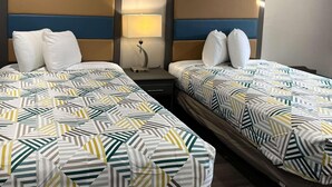 A hotel room with two beds, each with a patterned bedspread and white pillows. There is a nightstand with a lamp between the beds. - Motel6 Greenville, NC Ecu-medical Center (Greenville)