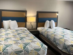 A hotel room with two beds, each with a patterned bedspread and white pillows. There is a nightstand with a lamp between the beds. - Motel6 Greenville, NC Ecu-medical Center (Greenville)