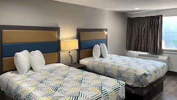 A hotel room with two beds, a window with curtains, and a wall-mounted air conditioning unit.