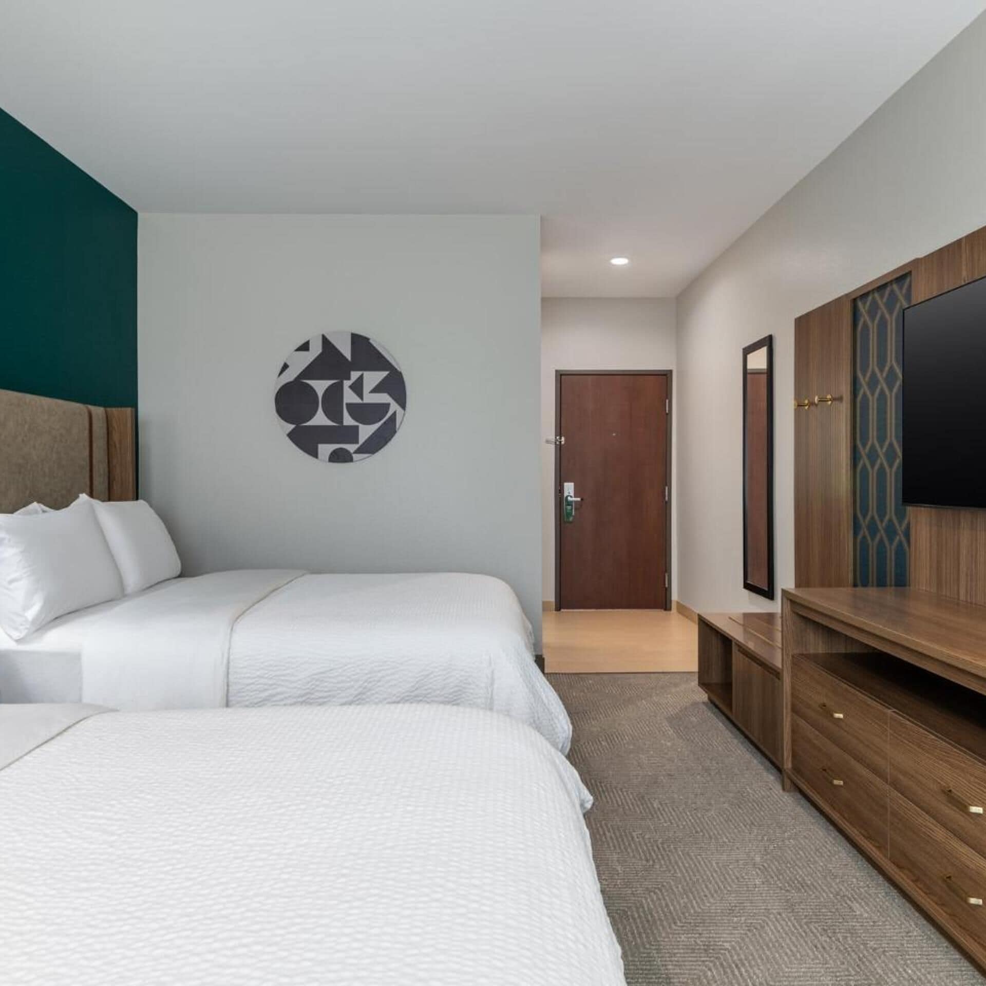 A hotel room with a bed, a wall-mounted TV, a wooden cabinet, and a door.