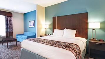 Een hotelkamer met een groot bed, een blauwe fauteuil, een kleine tafel en twee nachtkastjes met lampen.
