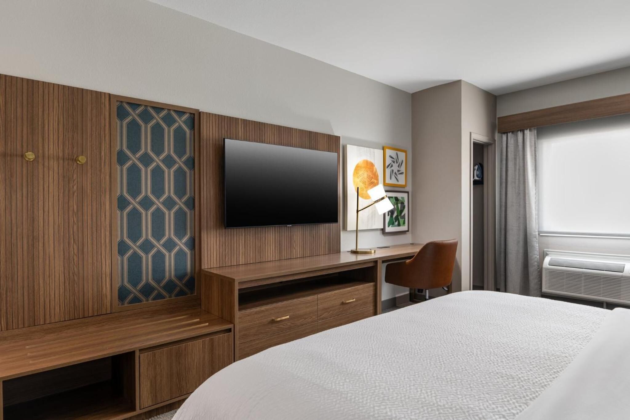 Habitación de hotel con cama, televisión, escritorio con silla, armario y ventana con cortinas.