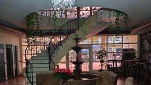A dining area with a round table, chairs, a chandelier, a spiral staircase, and a view of the outside.