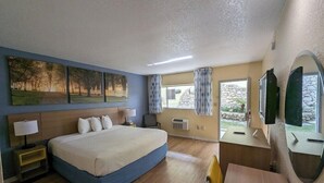 A hotel room with a bed, bedside tables, a desk, a chair, a TV, and a window with curtains.